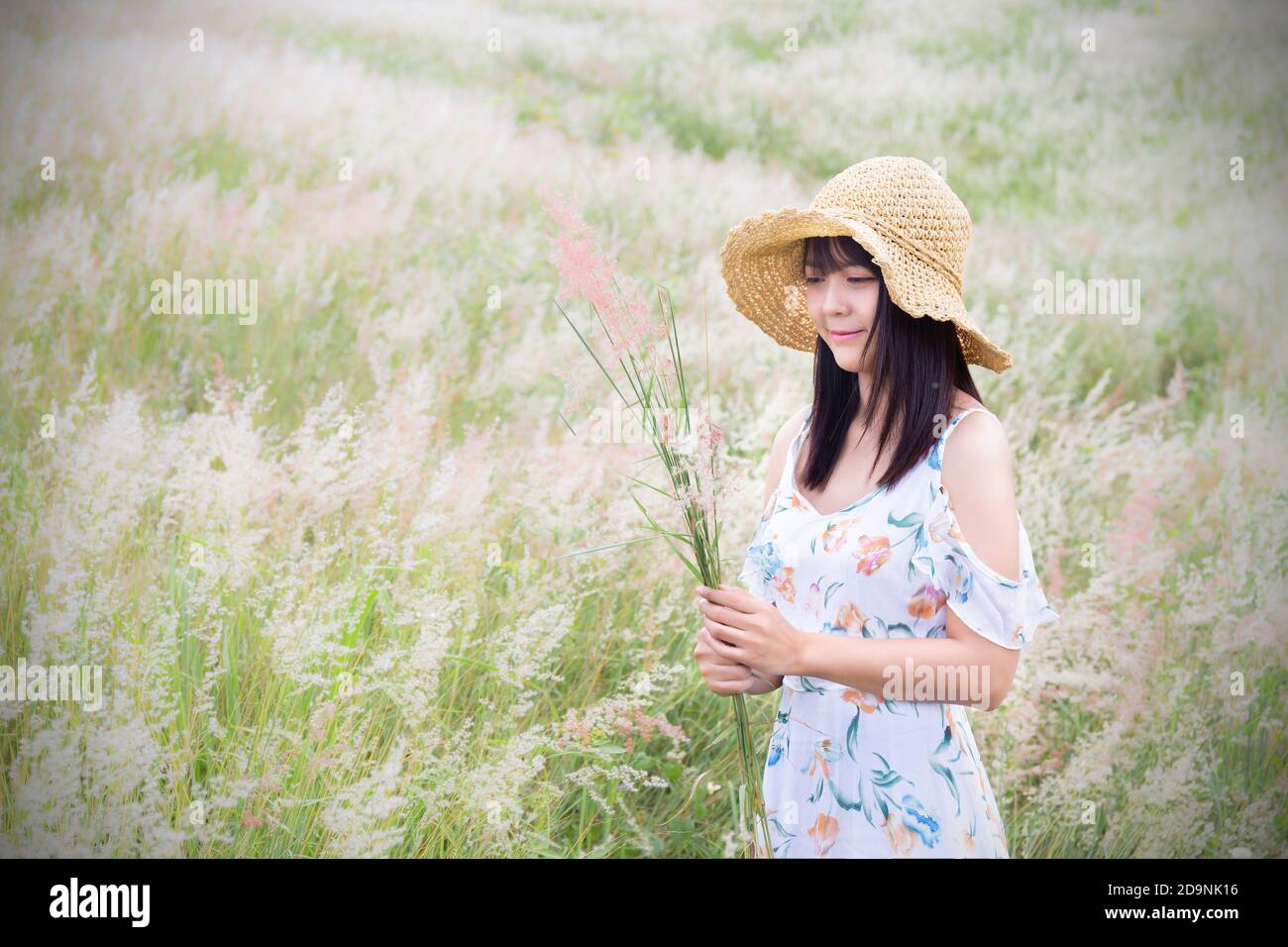 The girl wearing a hat, wearing a white dress, standing in the middle of the grass with beautiful white flowers with a relaxed and happy mood. Gray fr Stock Photo