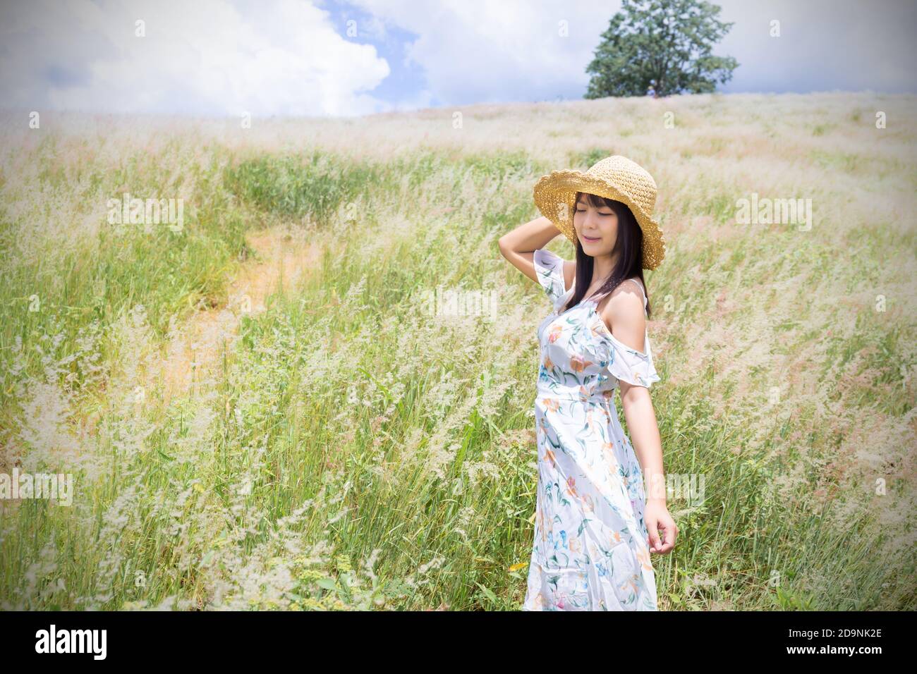 The girl wearing a hat, wearing a white dress, standing in the middle of the grass with beautiful white flowers with a relaxed and happy mood. Gray fr Stock Photo