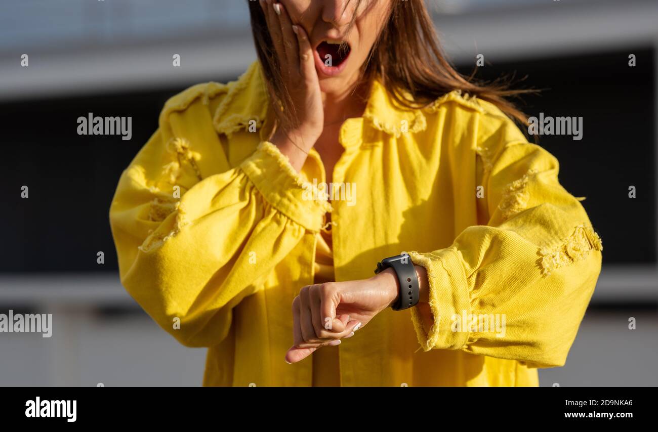 Young woman checking time on a smartwatch and feels shocked because of being late. Woman forgot about a meeting. Stock Photo