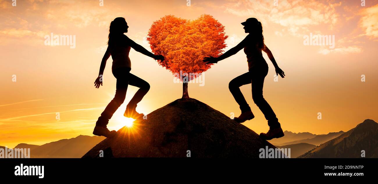 Two female silhouettes with a heart tree on a peak Stock Photo