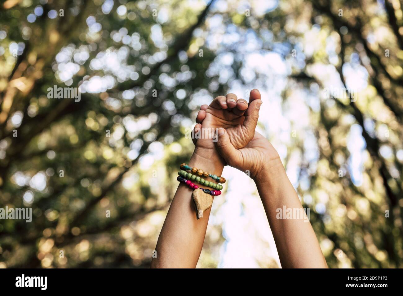 Hands with hippy bracelet with hearth and green forest trees background - concept of happy lifestyle and travel in the wild - people enjoying nature and freedom life Stock Photo
