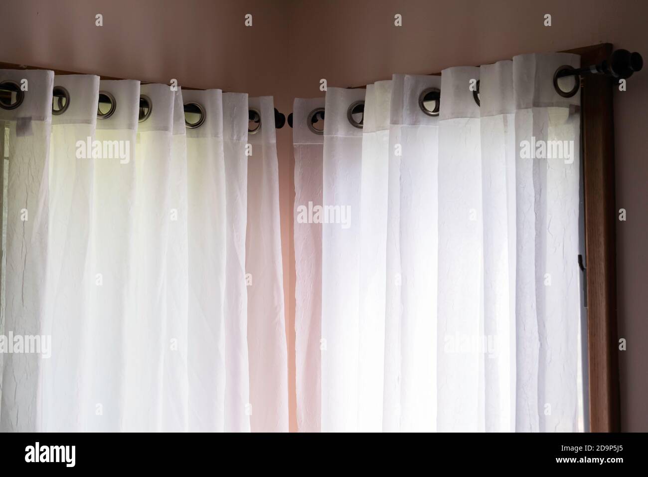 White semi-sheer curtains hanging from a decorative rod against peach walls. Stock Photo