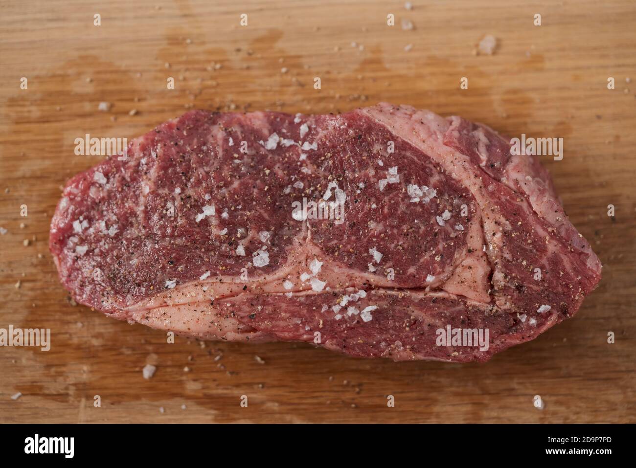 Raw ribeye steak spiced and ready to cook on oak board , shallow focus