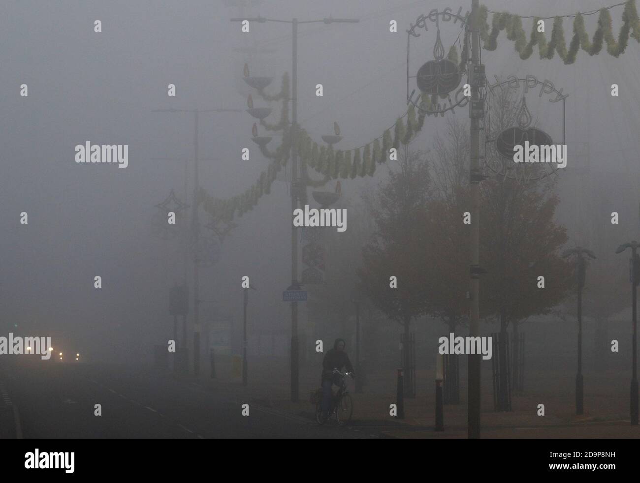 Leicester, Leicestershire, UK. 7th November 2020. UK weather.  A man cycles in fog under Diwali decorations during the second coronavirus pandemic lockdown. Credit Darren Staples/Alamy Live News. Stock Photo