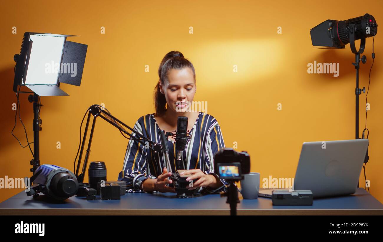 Influencer girl reviewing a new fluid head in professional studio. Social media star making online internet content about video equipment for web subscribers and distribution, digital vlog talking film Stock Photo