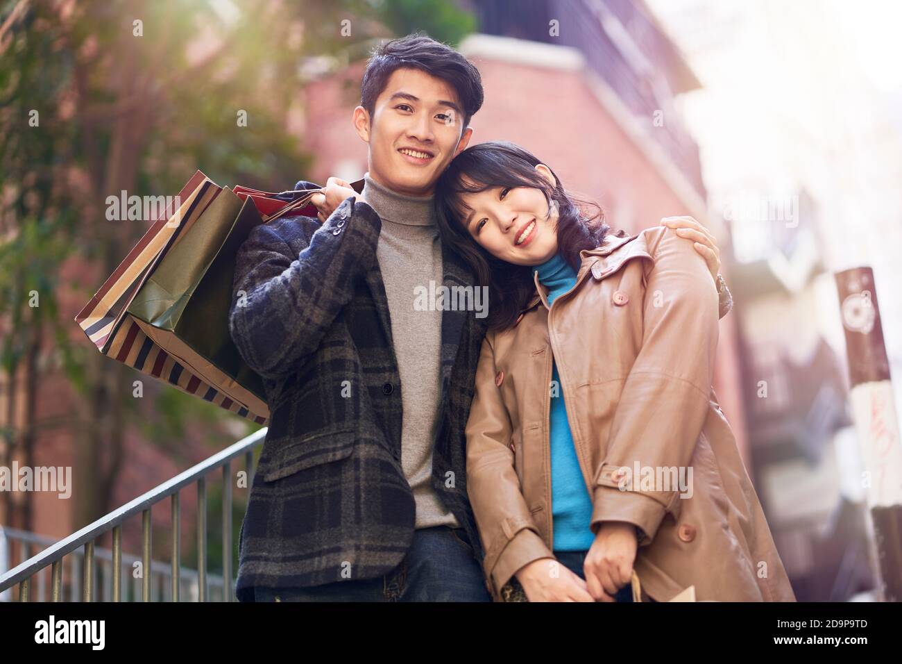 outdoor portrait of a happy young asian couple returning from a shopping spree, looking at camera smiling Stock Photo