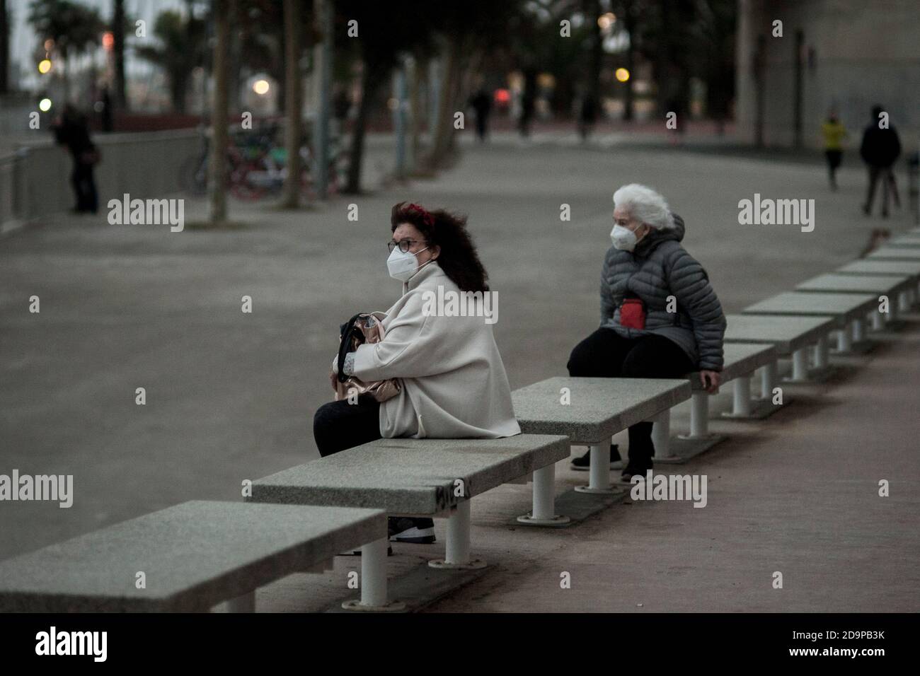Two women wearing face masks  sit  looking at the sea on the promenade of Barcelona. Coronavirus outbreak second wave in Spain, covid deaths over the last week came in at 1,002  and the infection rate  is starting to slow. Stock Photo