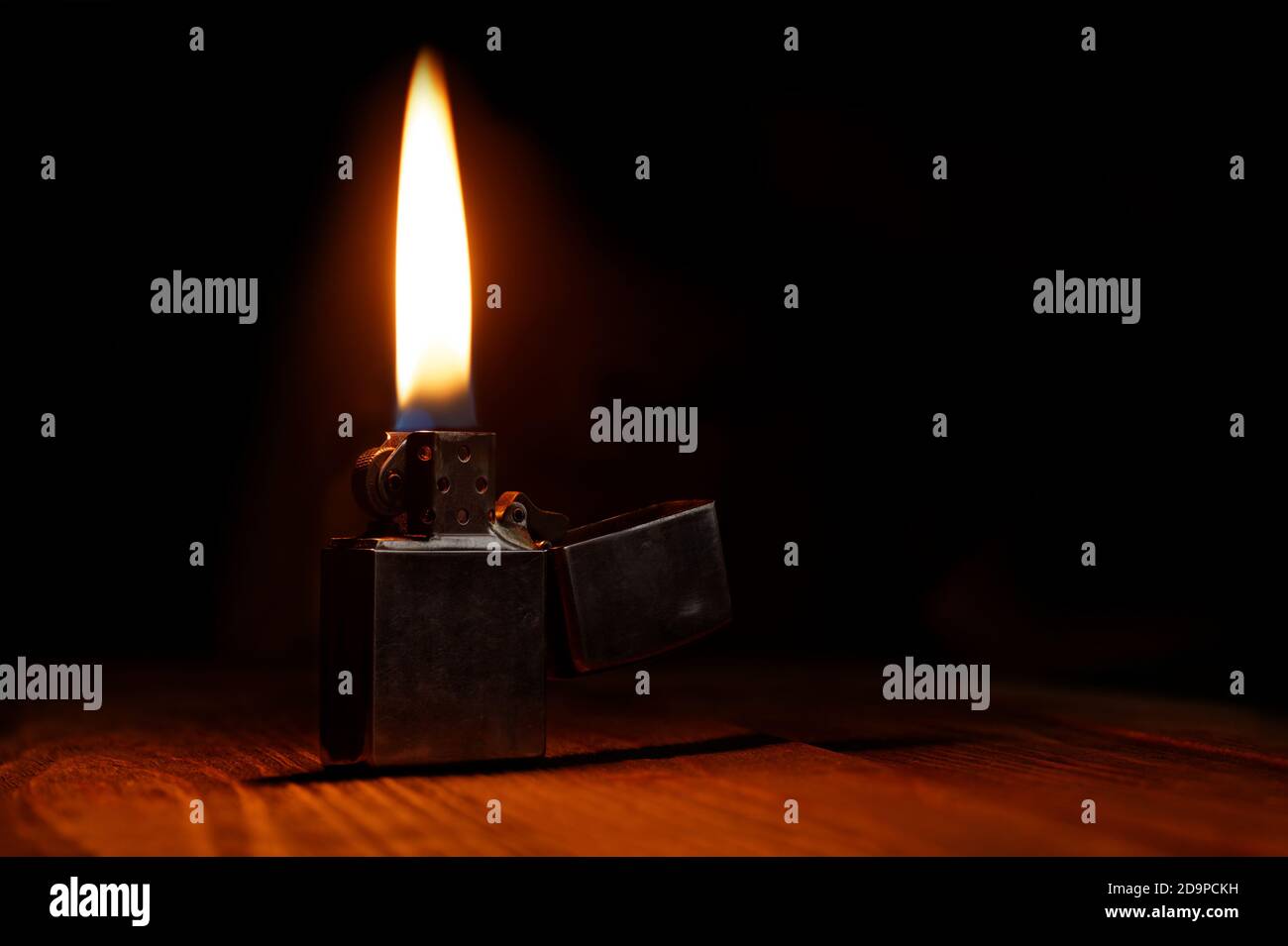 Old gasoline lighter with flame on wooden table against dark background Stock Photo