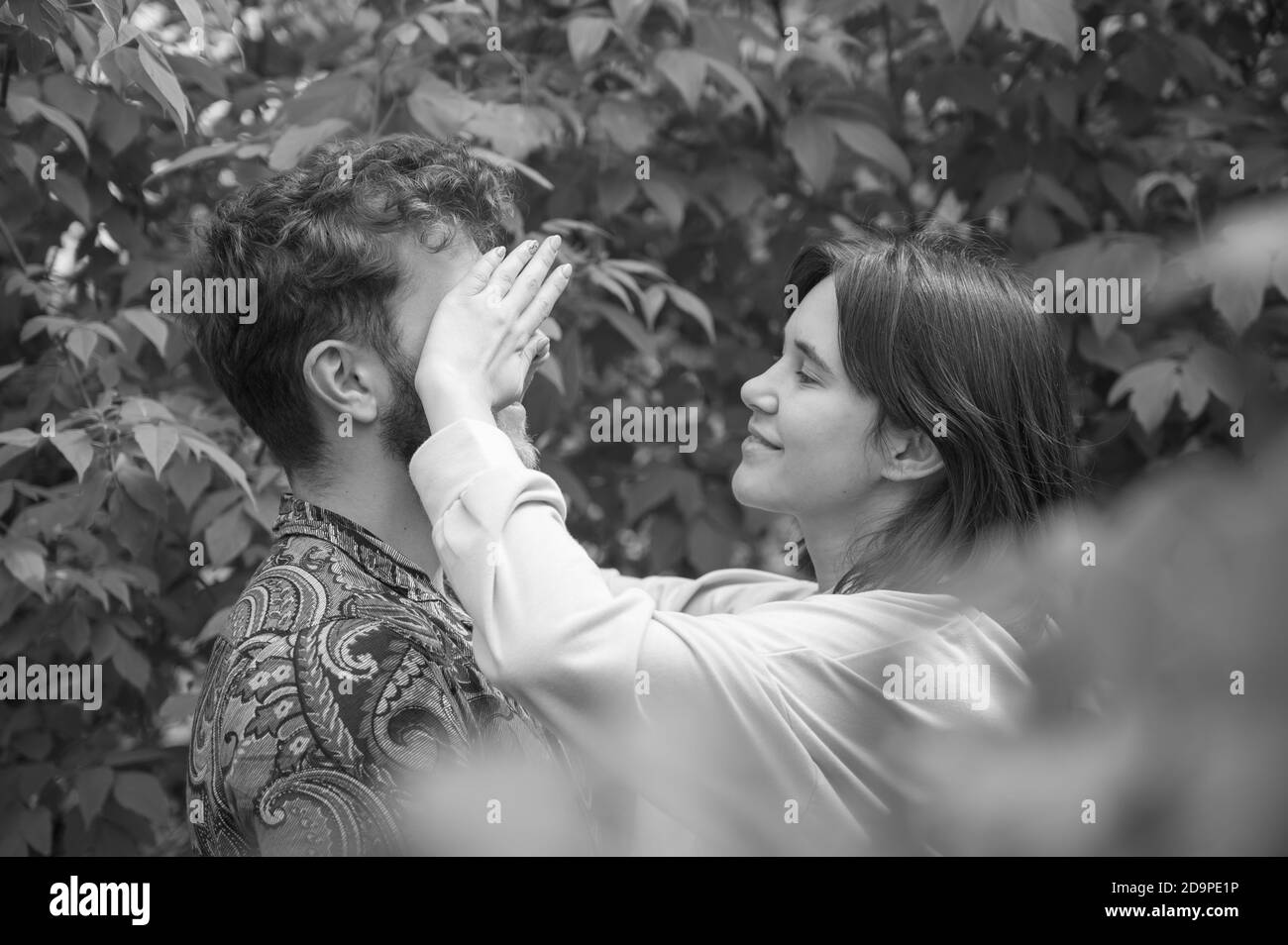 Black and white bright picture. Lovely young couple having fun. Girlfriend closes his eyes playing hide and seek. Beautiful casual woman and curly man Stock Photo