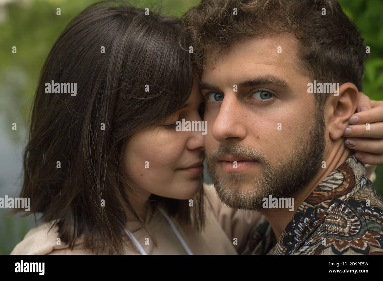Close up natural skin tones portrait of sweet young Ukrainian couple. Embrace and showing tenderness and love. Girlfriend hugs boyfriend while he look Stock Photo