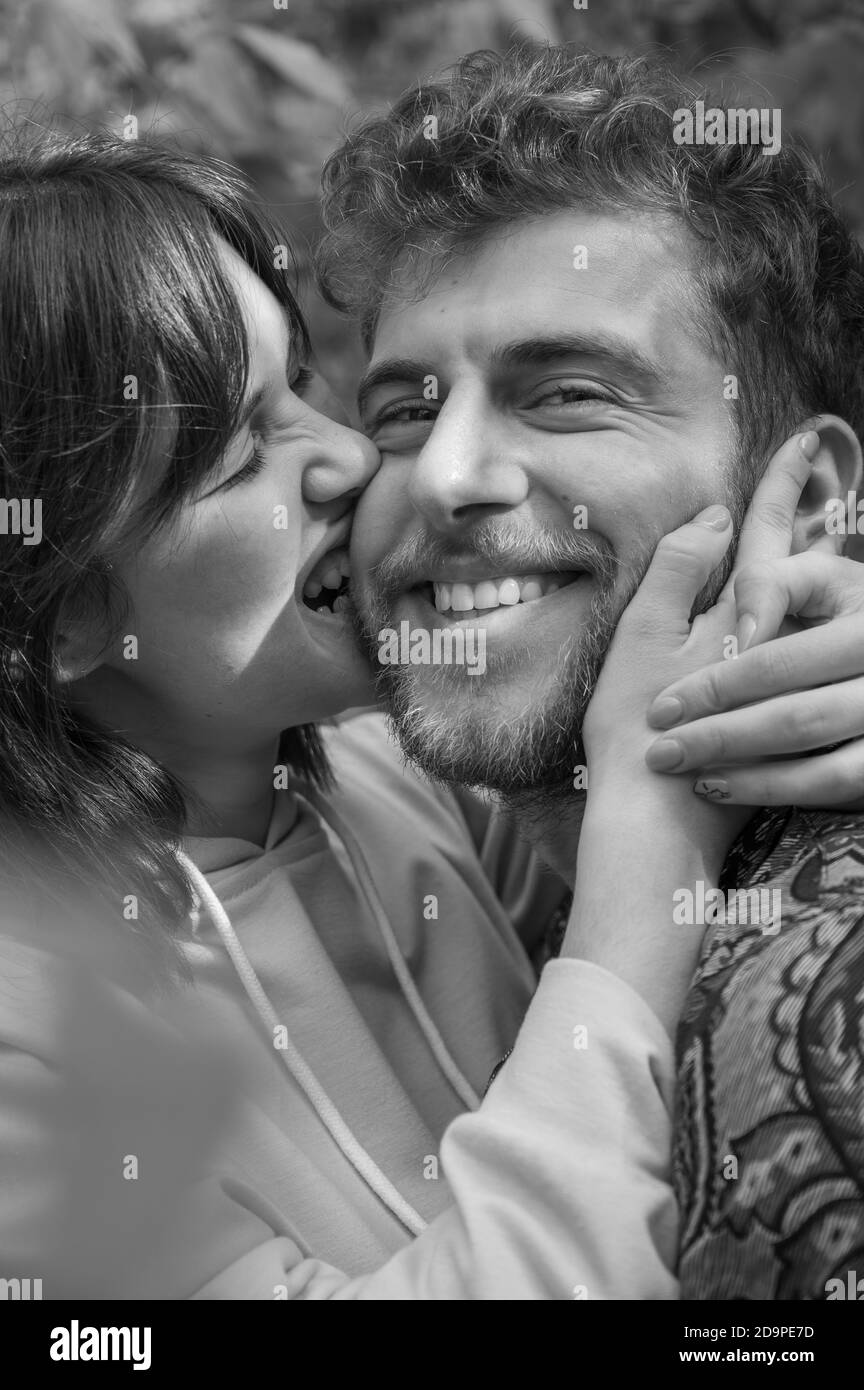 Black and white bright picture. Lovely young couple having fun. Girlfriend bites his cheek and boyfriend smiles. Beautiful casual woman and curly man Stock Photo