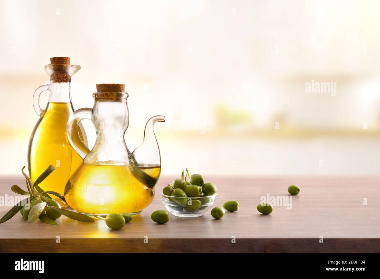 Olive oil in two glass containers and harvest olives on the wooden bench in a kitchen. Front view. Stock Photo