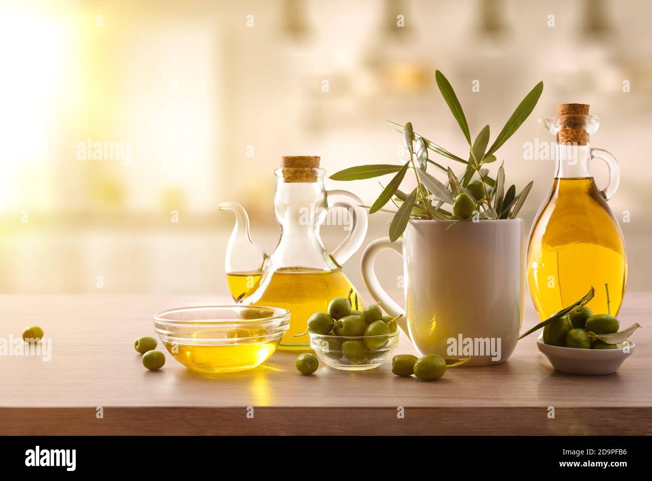 Virgin olive oil in two glass containers and harvest olives on the wooden bench in a kitchen. Front view. Stock Photo