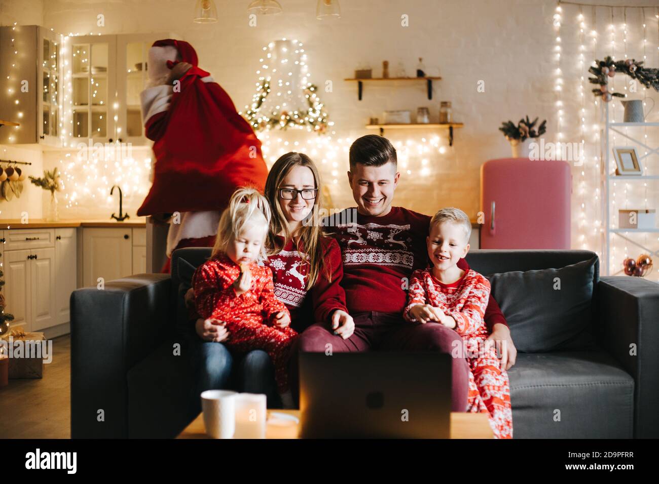 Santa Claus putting gifts under Christmas tree in room with family ...