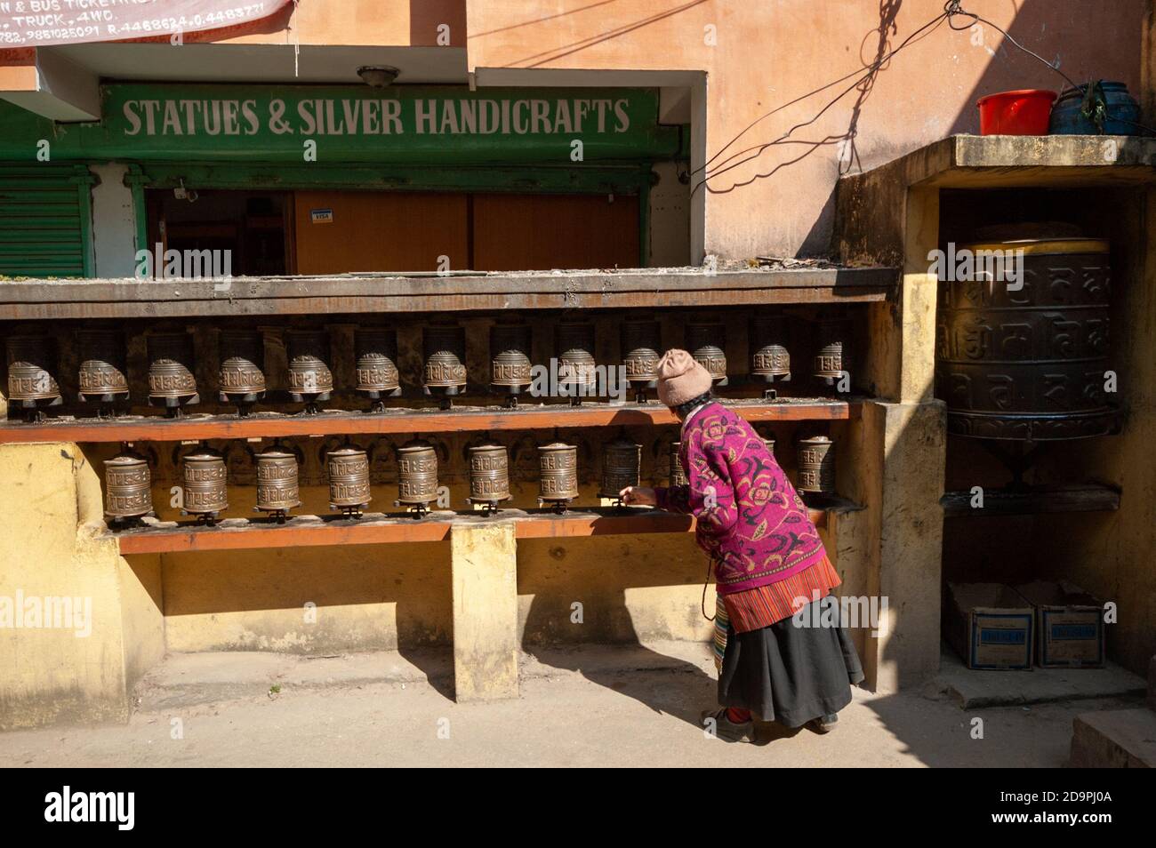 A woman spins prayer wheels at Kathmandu's largest buddhist stupa Boudhanath in front of a handicraft shop Stock Photo