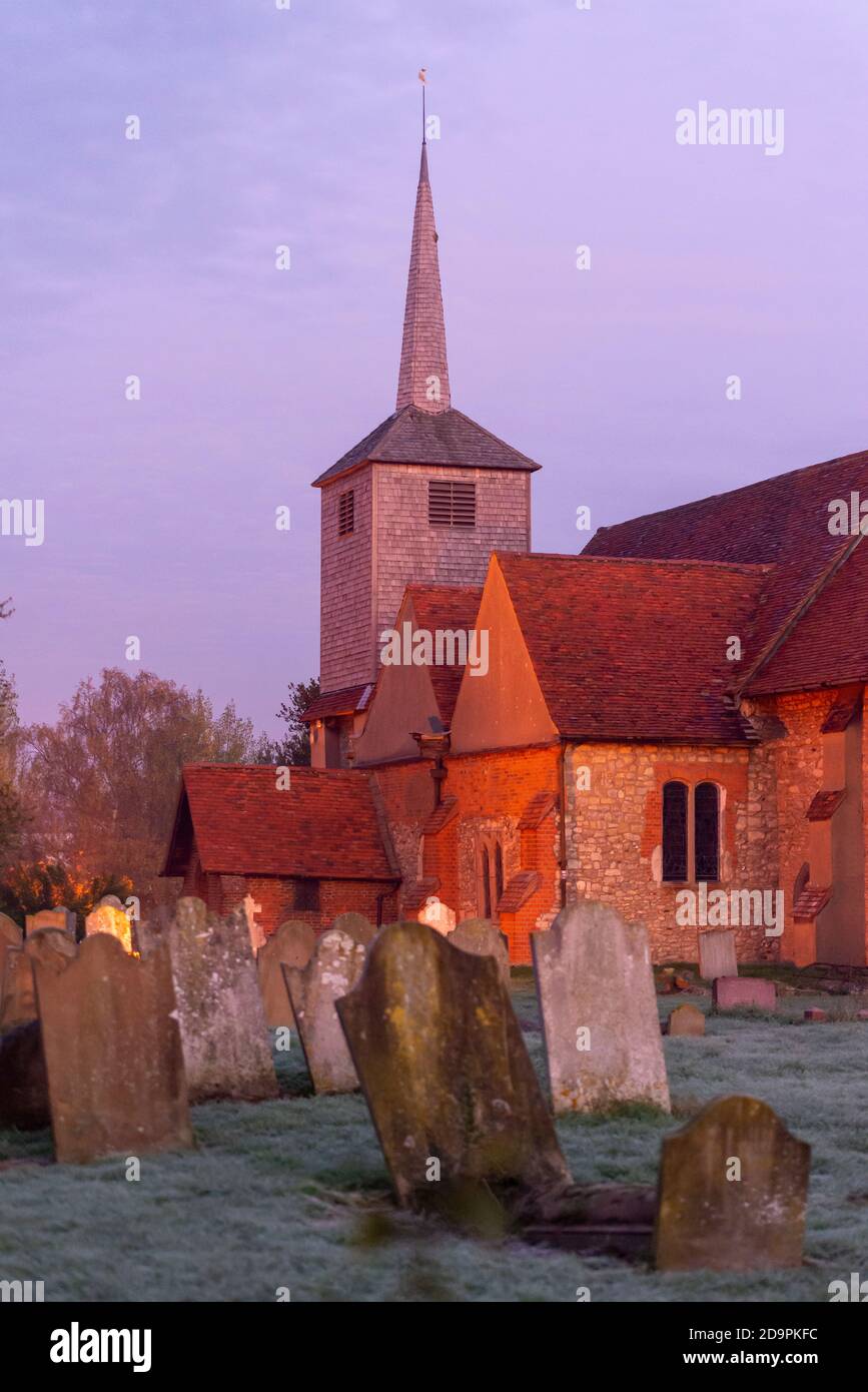 St Laurence and All Saints Church in Eastwood, Southend on Sea, Essex, UK, at dawn with warm glow. Grave headstones Stock Photo
