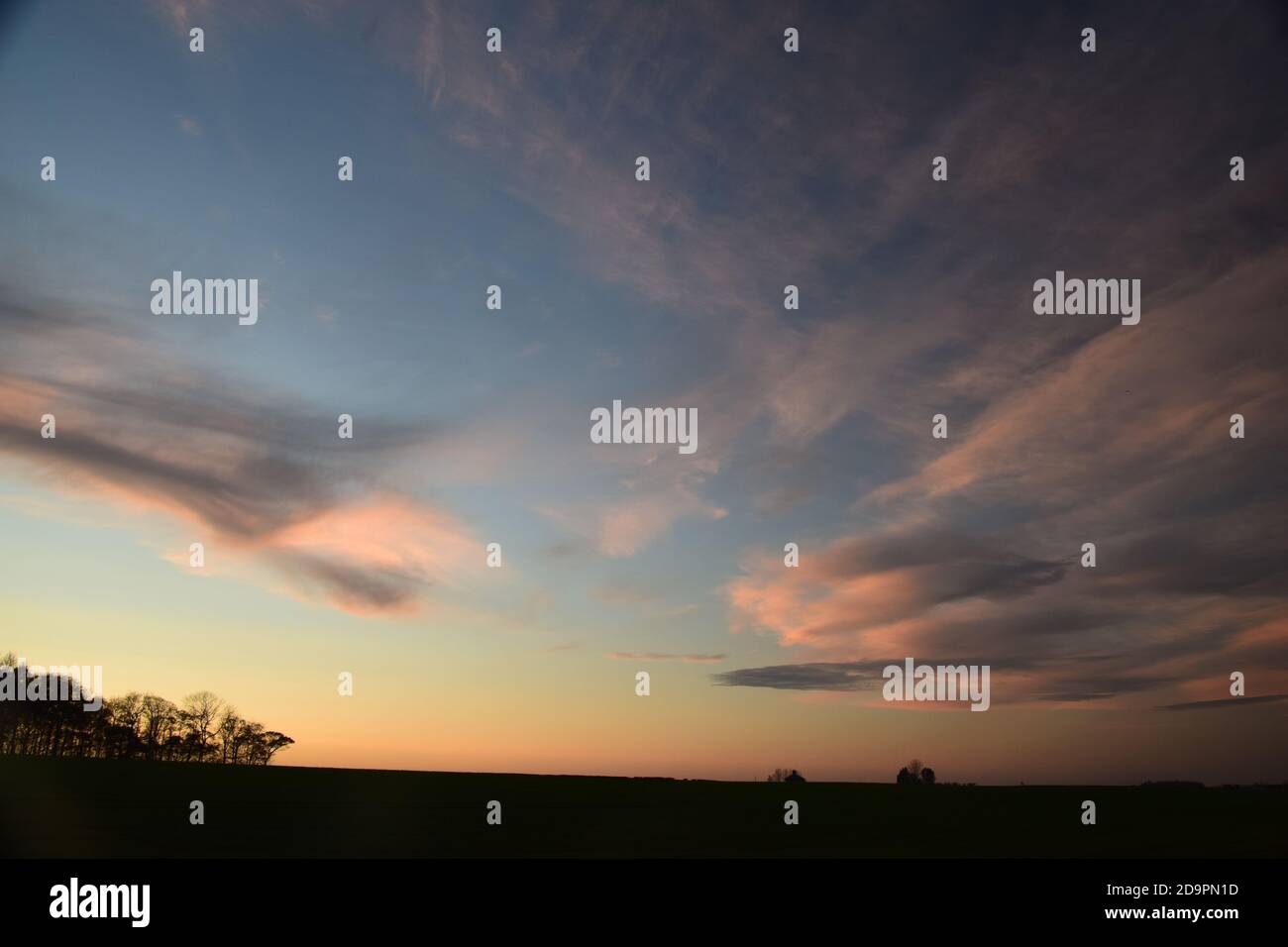 Cirrus type clouds tinged with colour from the setting sun highlighting shapes and patterns across the sky. Stock Photo