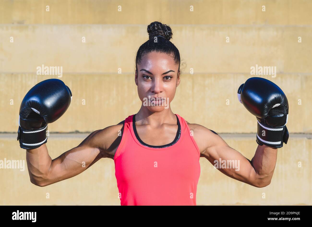 young attractive afro american boxer woman wearing black and pink sportswear looking at the camera and defiantly showing her muscular biceps Stock Photo