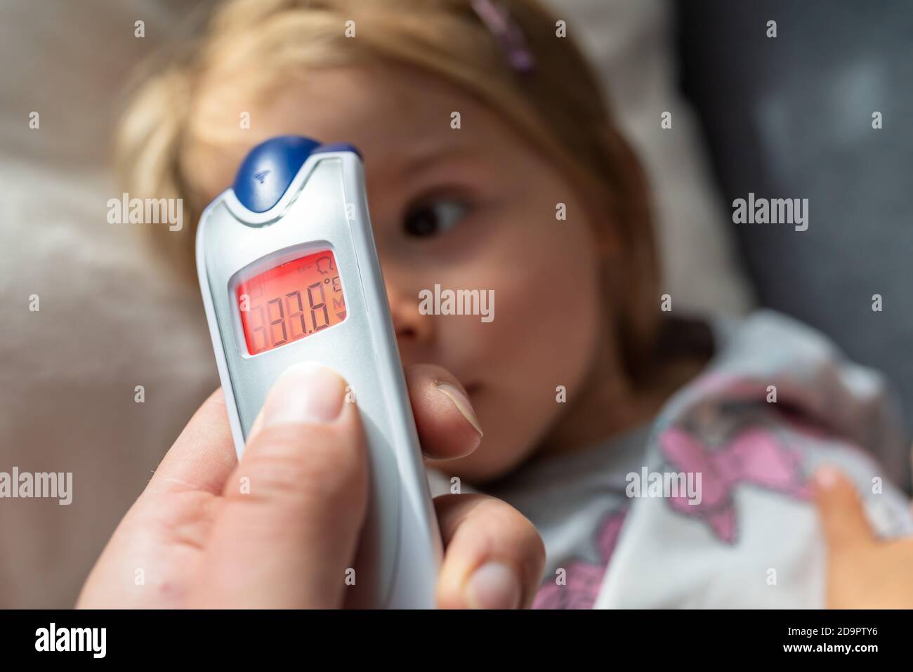 Parent takes temperature for her child with infrared thermometer at home, low-grade fever Stock Photo