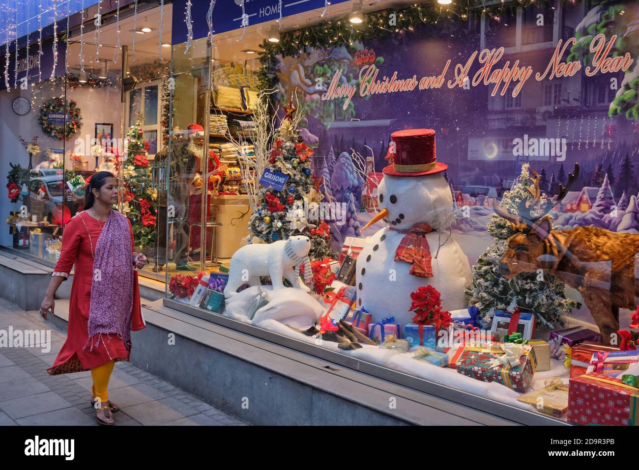 An Indian woman in Colaba, Mumbai, India, passes a shop window with Western-style Christmas decoration including a snowman and Christmas tree Stock Photo