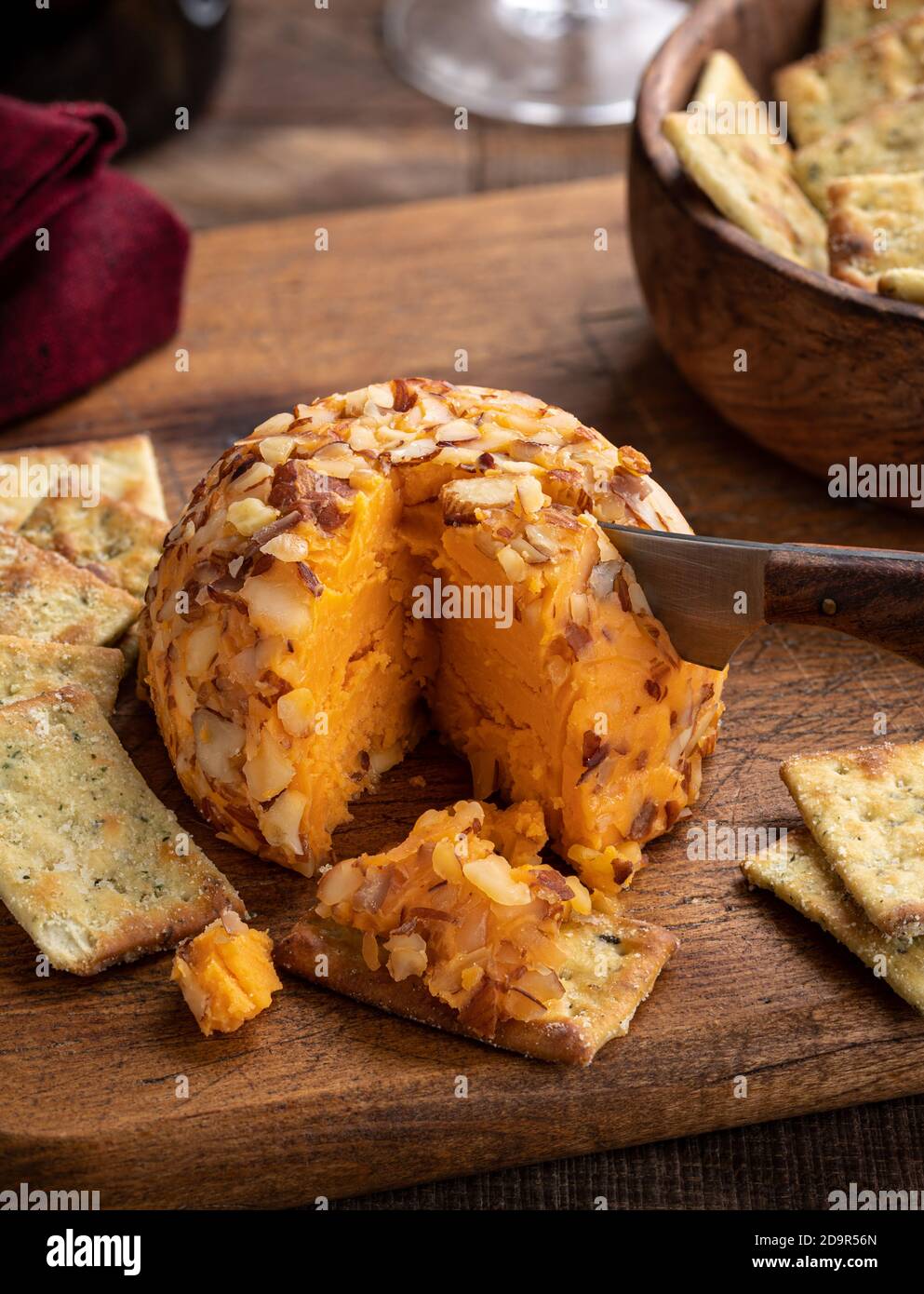 Cheddar cheese ball cut with a knife and spread on a cracker on a rustic wooden cutting board Stock Photo