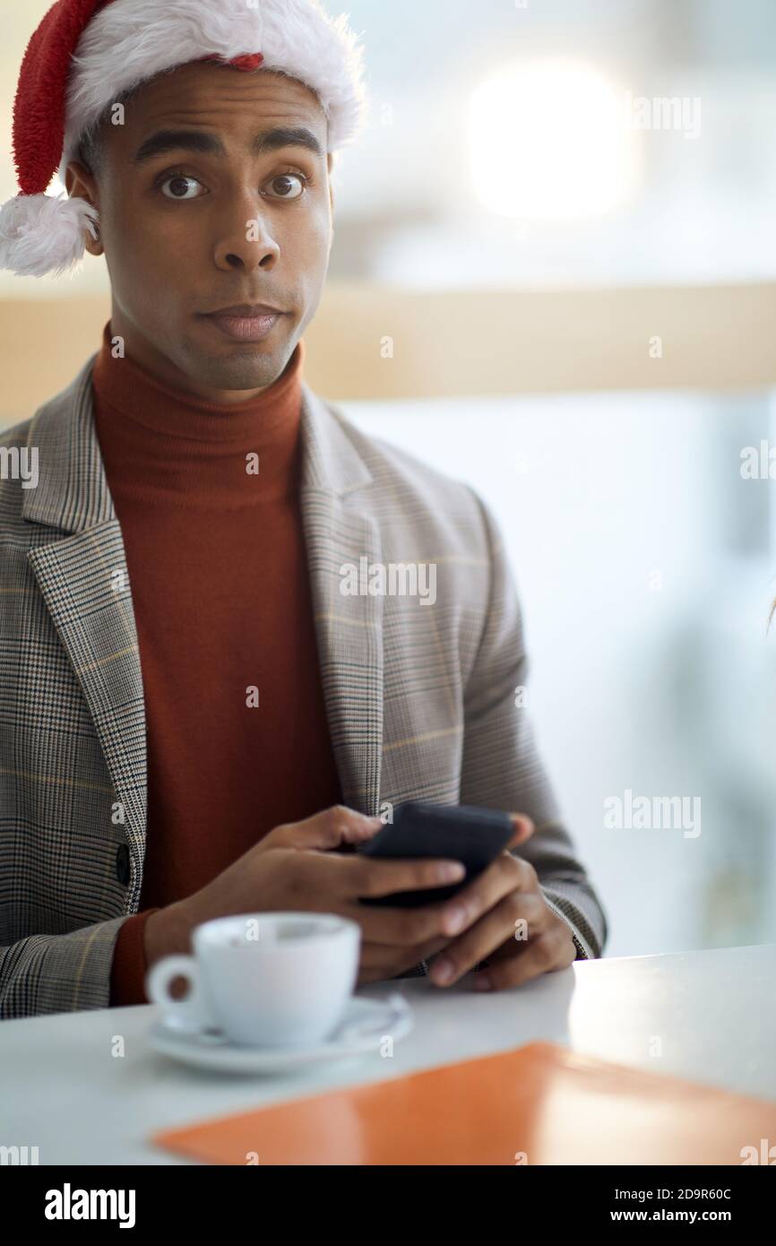 surprised look of young afro-american in the office, texting on cell phone, wearing santa hat Stock Photo