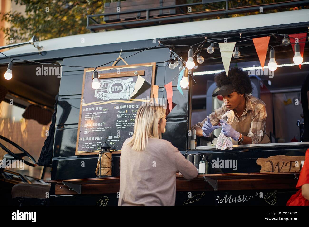 afro-american employee showing size of a fast food mealto a caucasian customer from a window of modified truck for mobile fast food Stock Photo