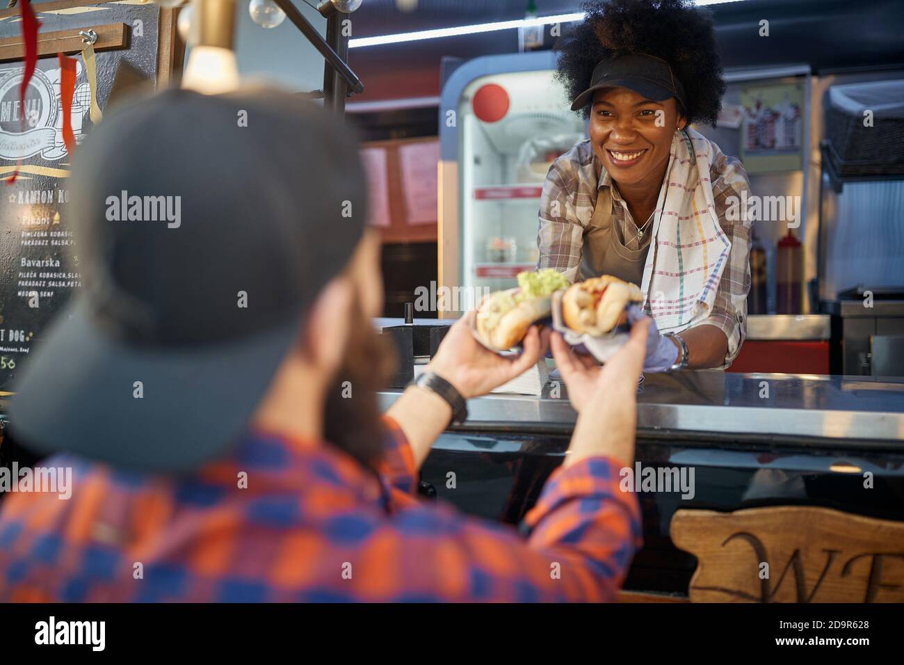 close up of sandwiches with green salad and mustard. caucasin male receiving from a smiling afro-american employee in fast food service Stock Photo