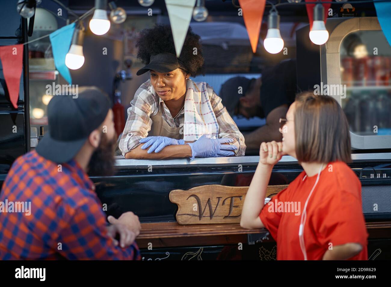 afro-american female employee in fast food service looking at male customer with smile, listening Stock Photo