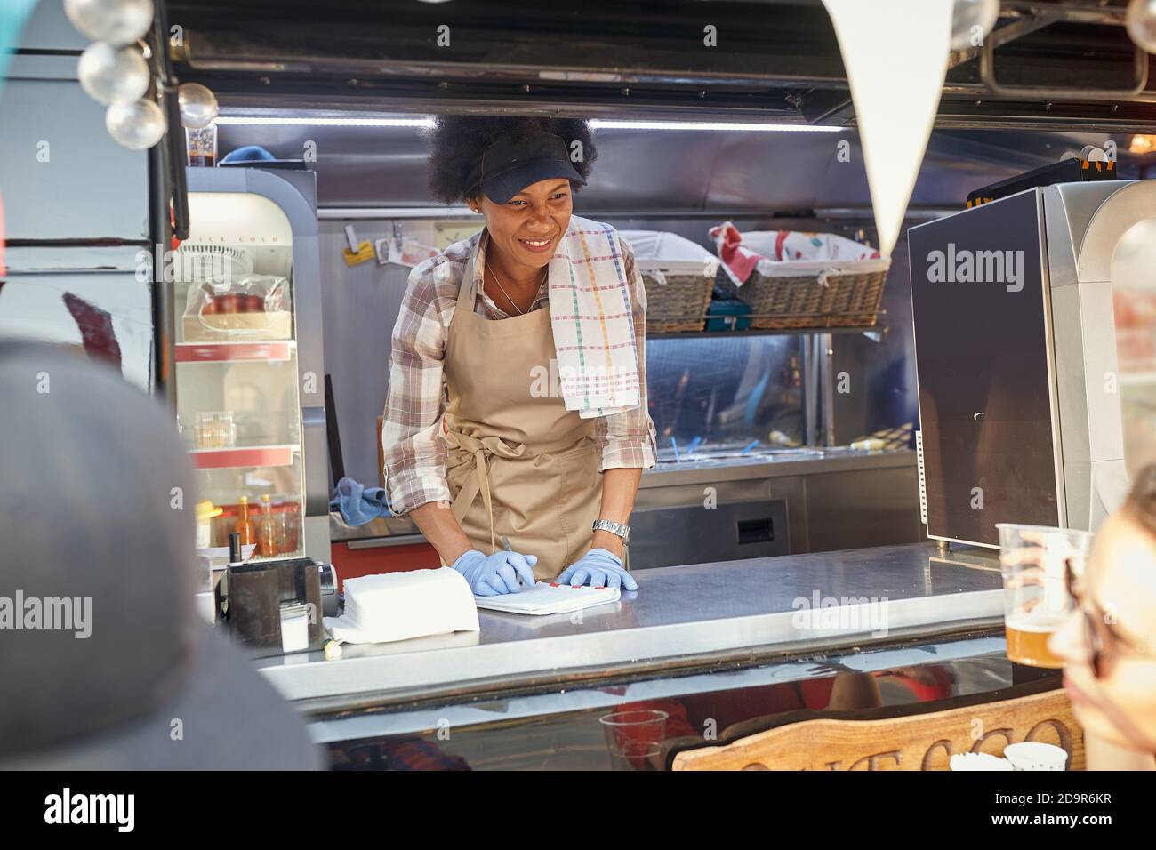 young afro-american female employee in fast food service writing down the order looking at customer holding beer Stock Photo