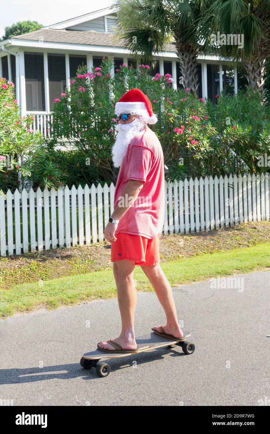 Dressed as beach Santa a man rides a skateboard in the annual Independence Day parade July 4, 2019 in Sullivan's Island, South Carolina. The tiny affluent Sea Island beach community across from Charleston holds an outsized golf cart parade featuring more than 75 decorated carts. Stock Photo