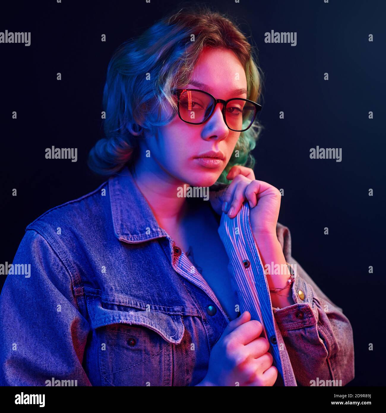 Portrait of young alternative girl in glasses with green hair in red and blue neon light in studio Stock Photo