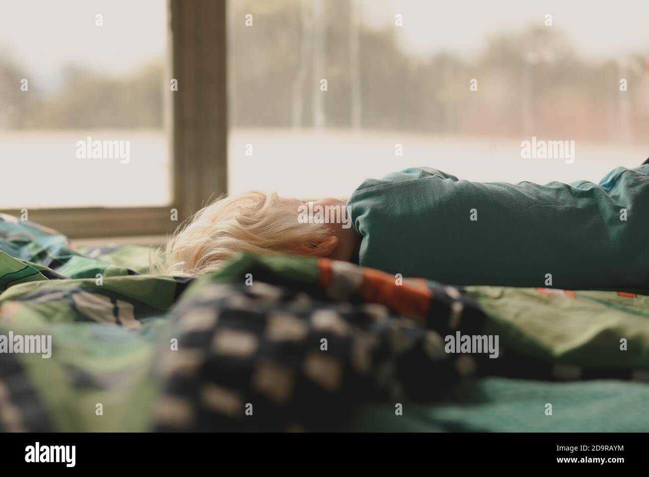 Little kid sleeping in a bed by the window on a rainy day Stock Photo