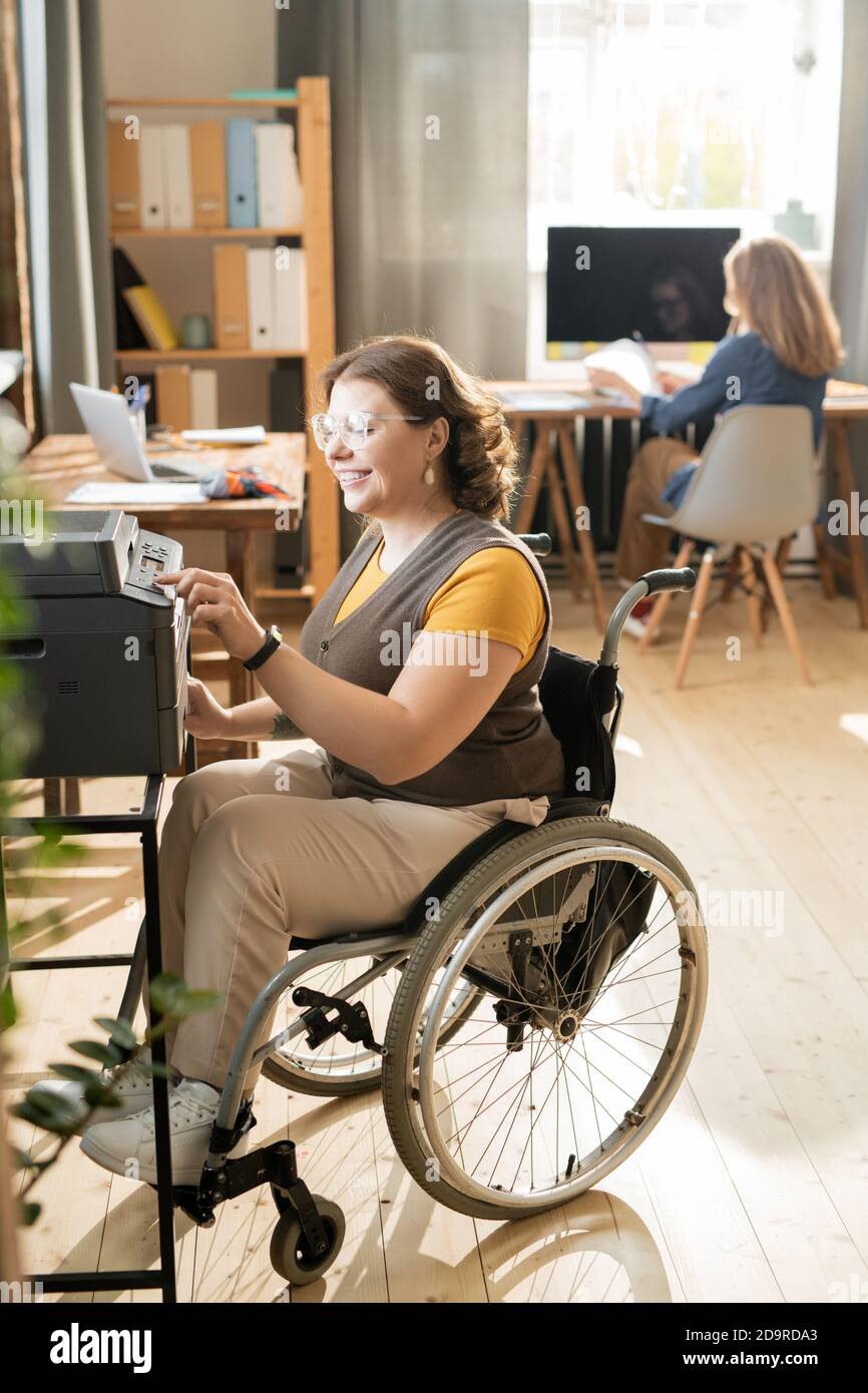 Happy young disable female in wheelchair pressing start button of xerox machine Stock Photo