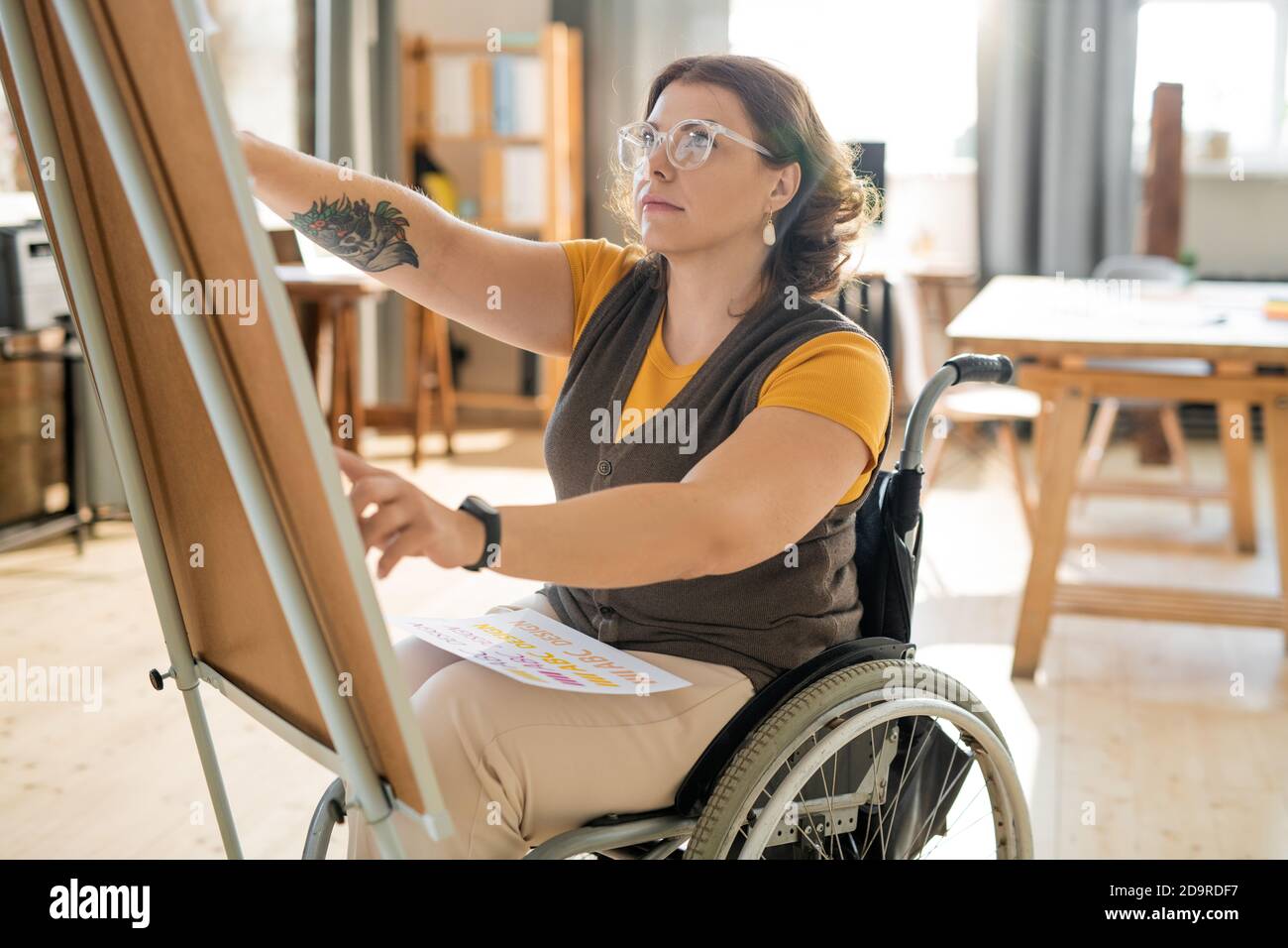 Young female coach in casualwear sitting in wheelchair in front of whiteboard Stock Photo