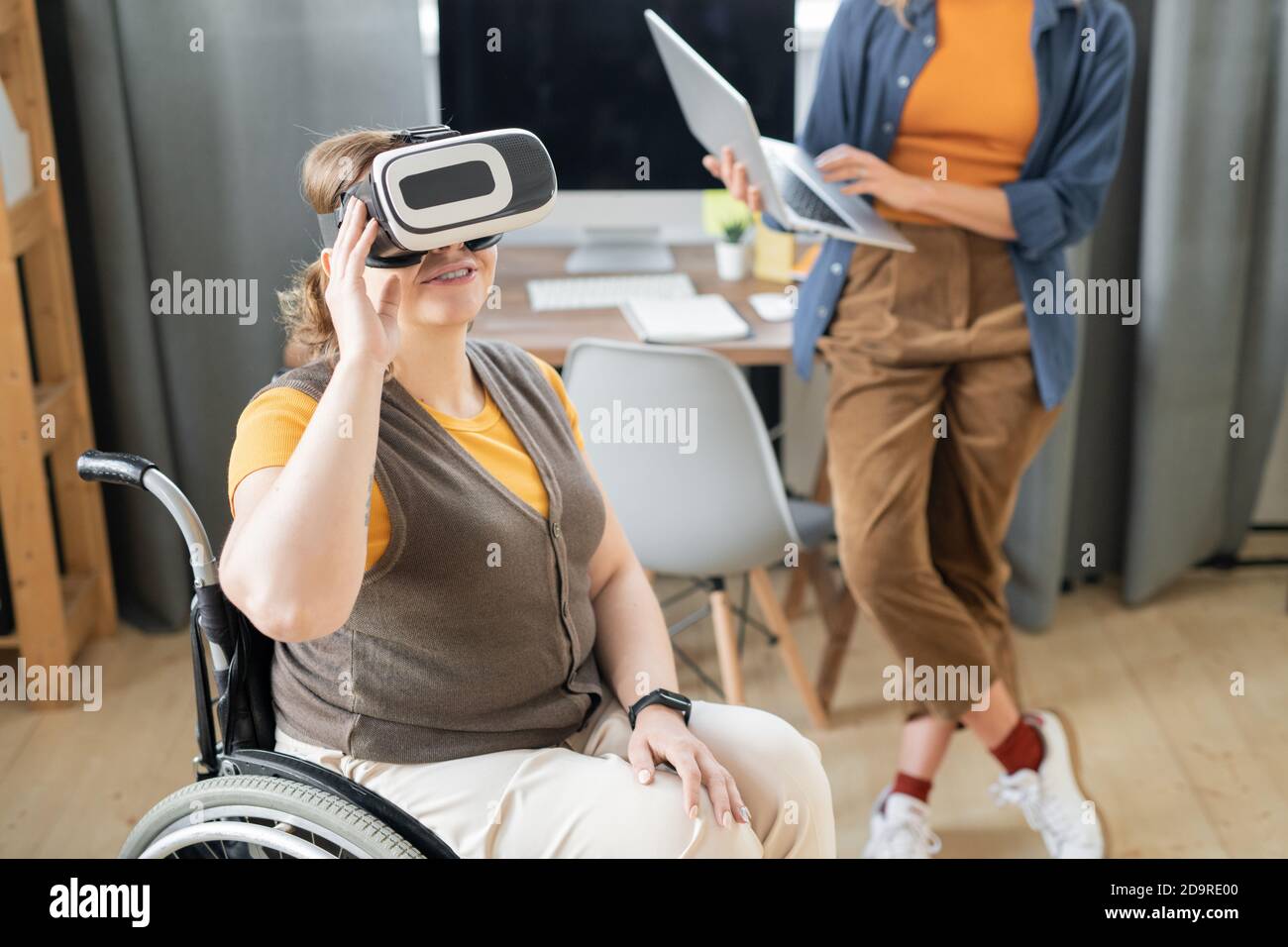 Disable businesswoman in vr headset sitting in wheelchair against busy colleague Stock Photo