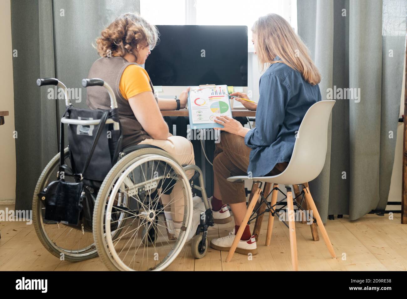 Two young contemporary female office workers discussing financial papers Stock Photo