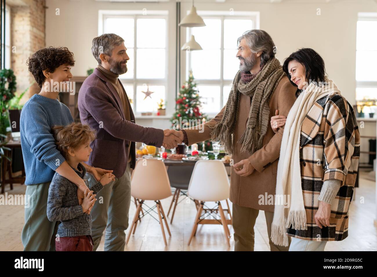 Happy young and mature couples greeting each other during Christmas visit Stock Photo