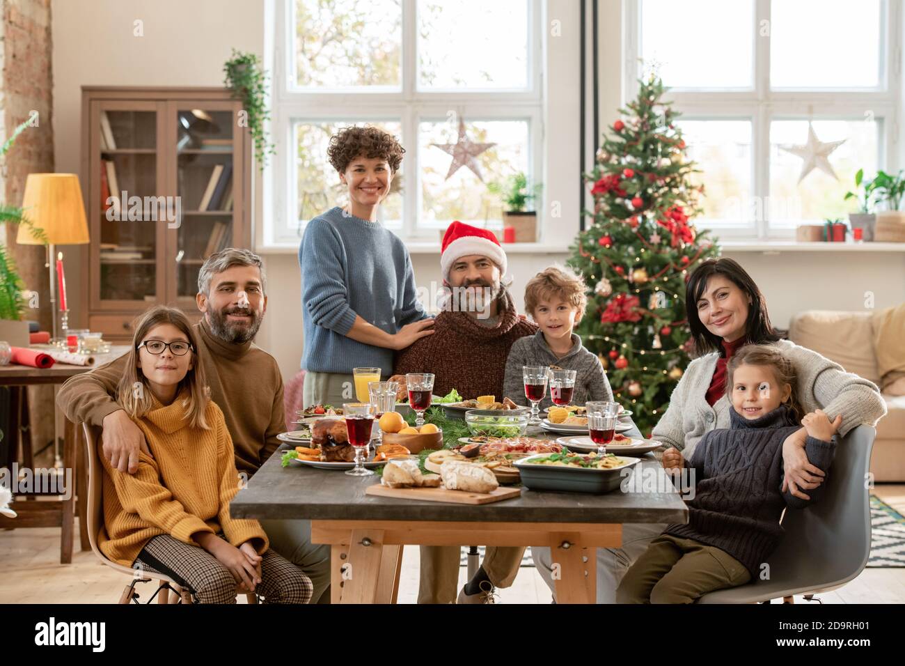 Happy young and mature couples and three cute kids gathered by festive table Stock Photo