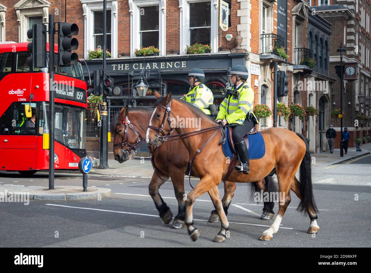 British mounted police officers in Whitehall, Westminster, London, UK, riding past a pub and a red London bus. English police in London on horses Stock Photo