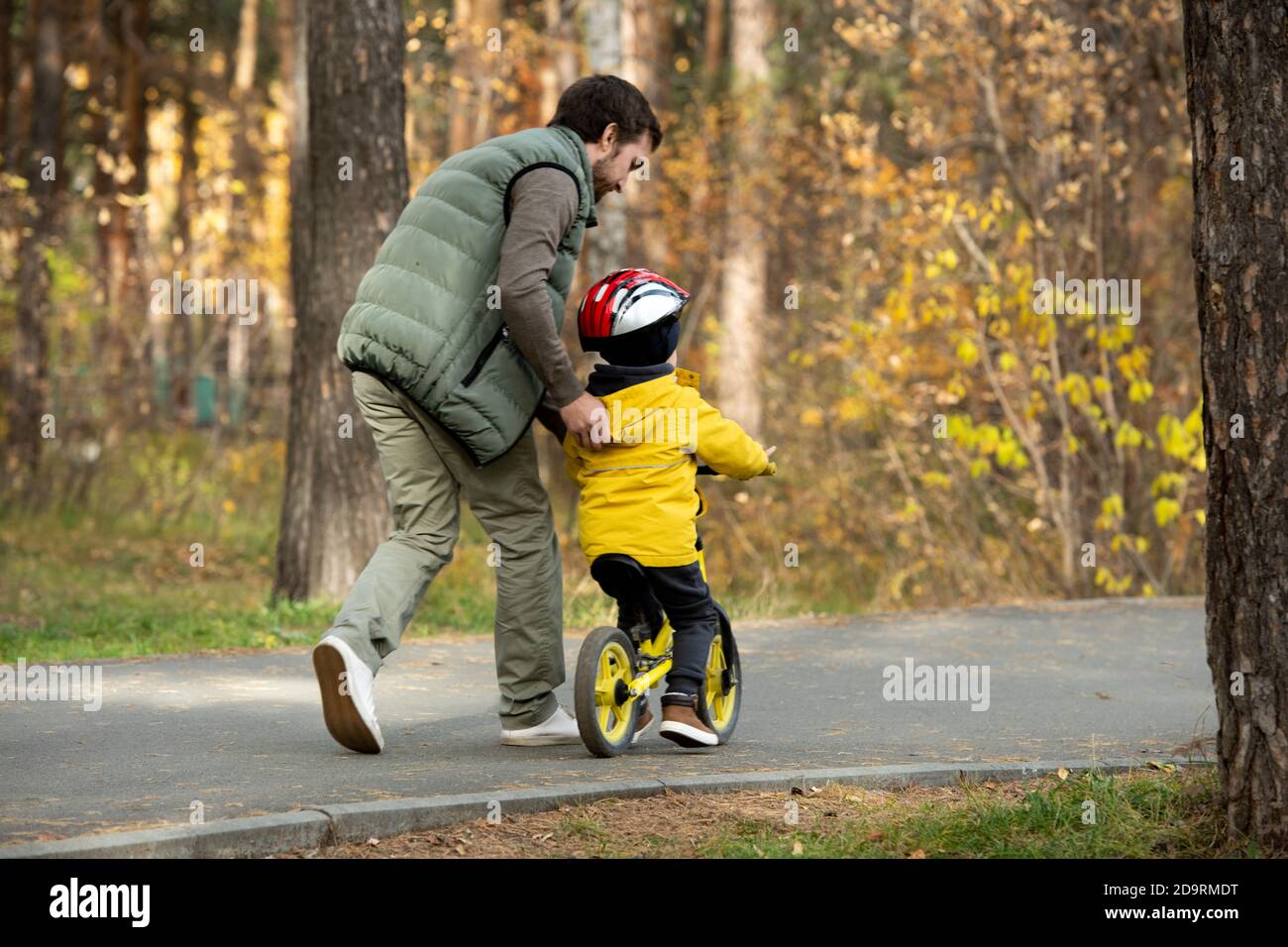 Rear view of young man running after his active little son riding balance bike Stock Photo