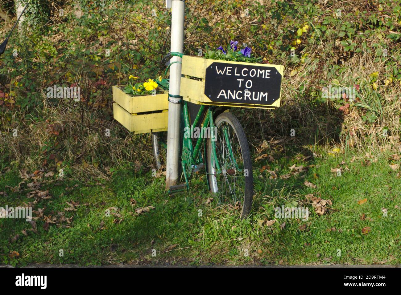 Welcome to Ancrum sign on a wooden flower box on a bicycle beside a signpost, Roxburghshire, Scottish Borders, Scotland, UK. Stock Photo