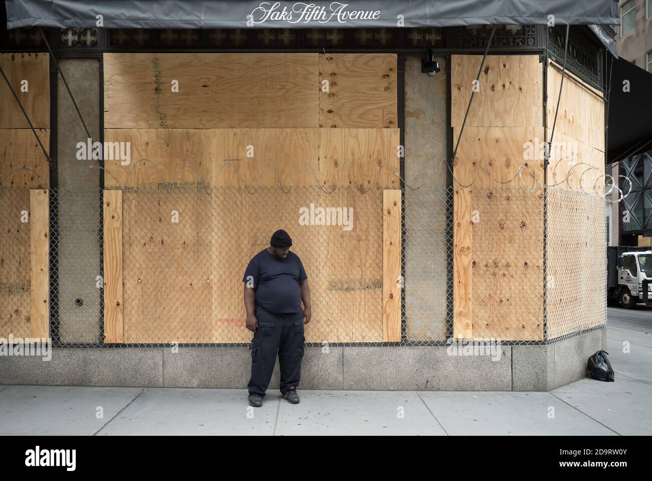 Exhausted security man stands in front of one of Saks Fifth Avenue boarded up windows Stock Photo