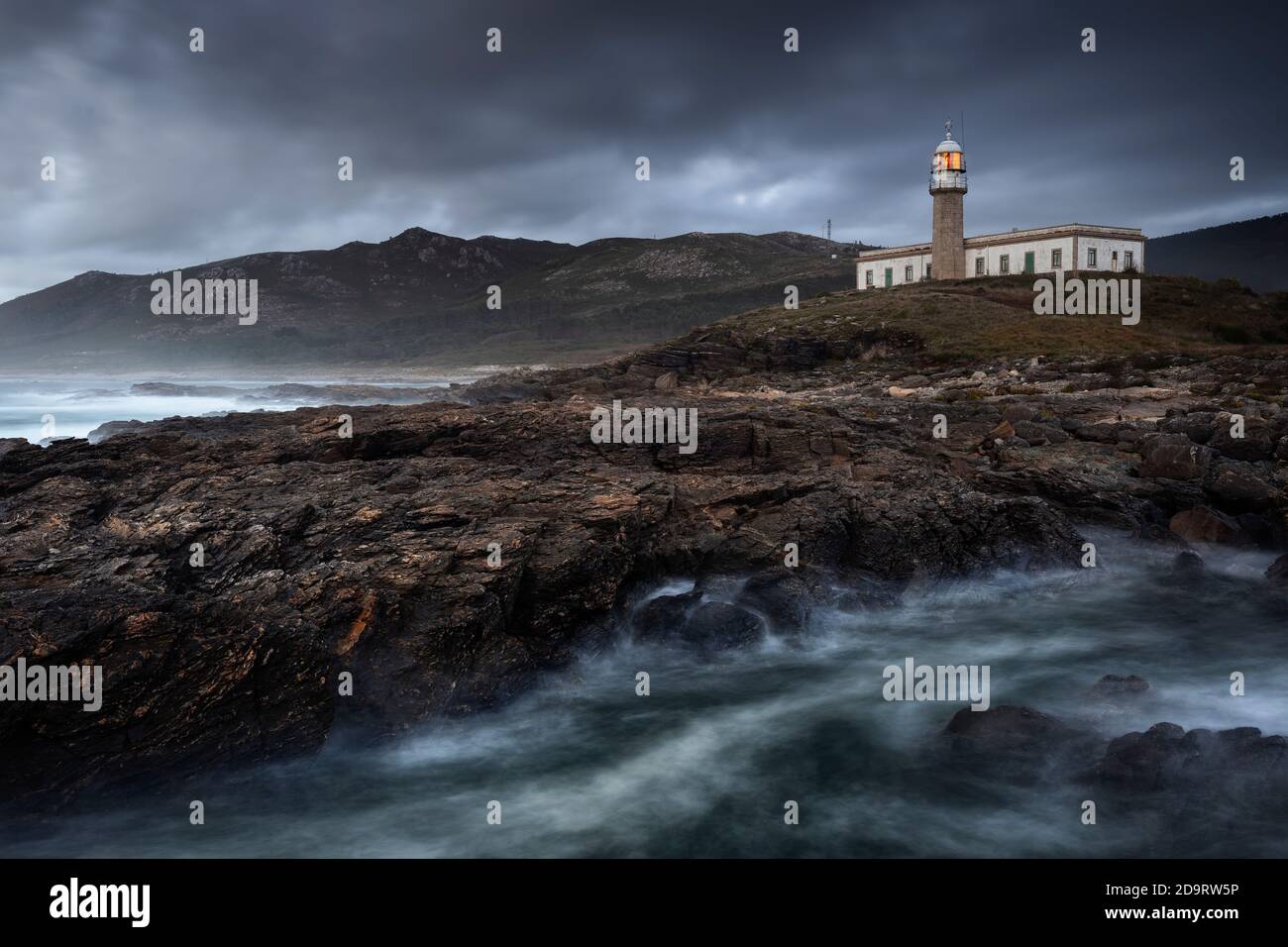 Lighthouse on the cliff with a dramatic sky and wild waters nearby Stock Photo