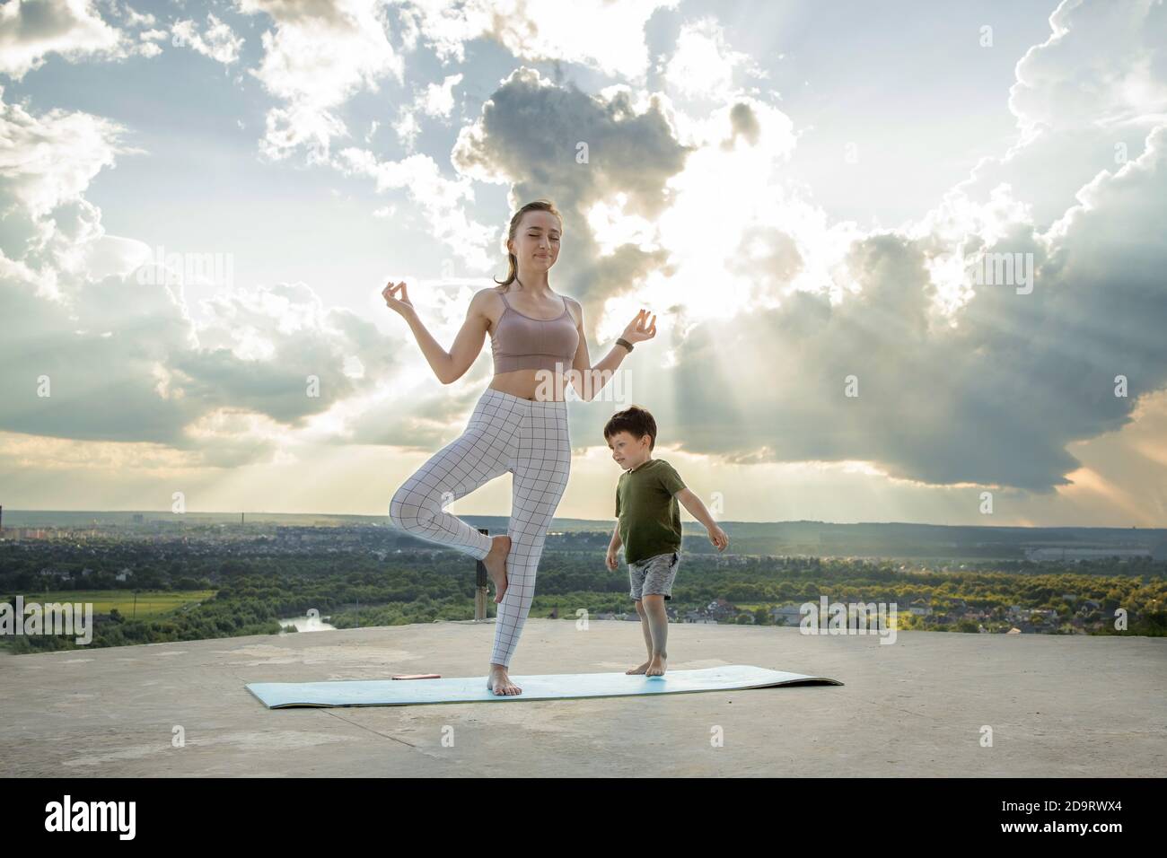 Mother and son doing exercise on the balcony in the background of a city during sunrise or sunset, concept of a healthy lifestyle Stock Photo