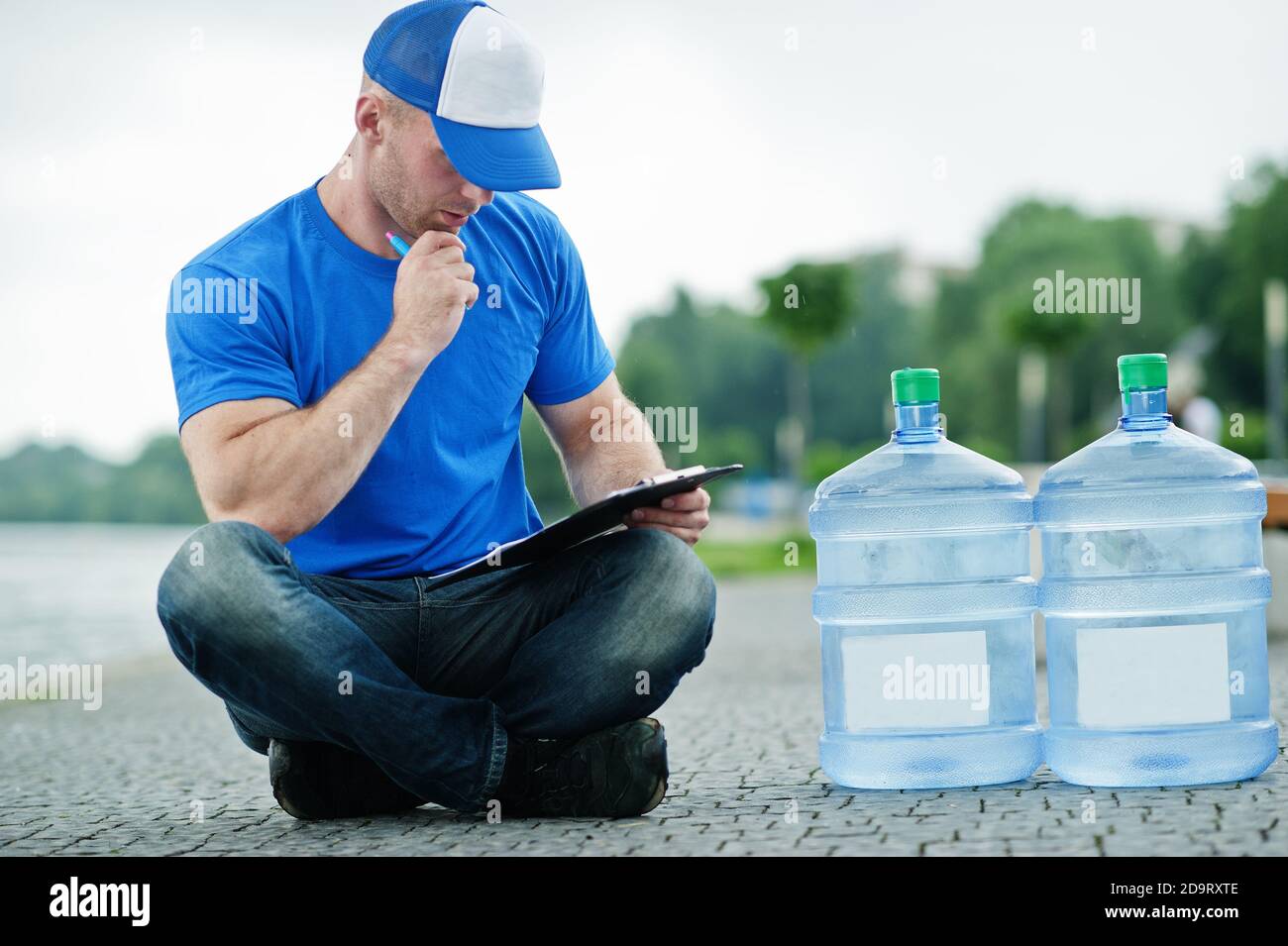 Delivery man sitting with clipboard water bottles outdoor. Stock Photo