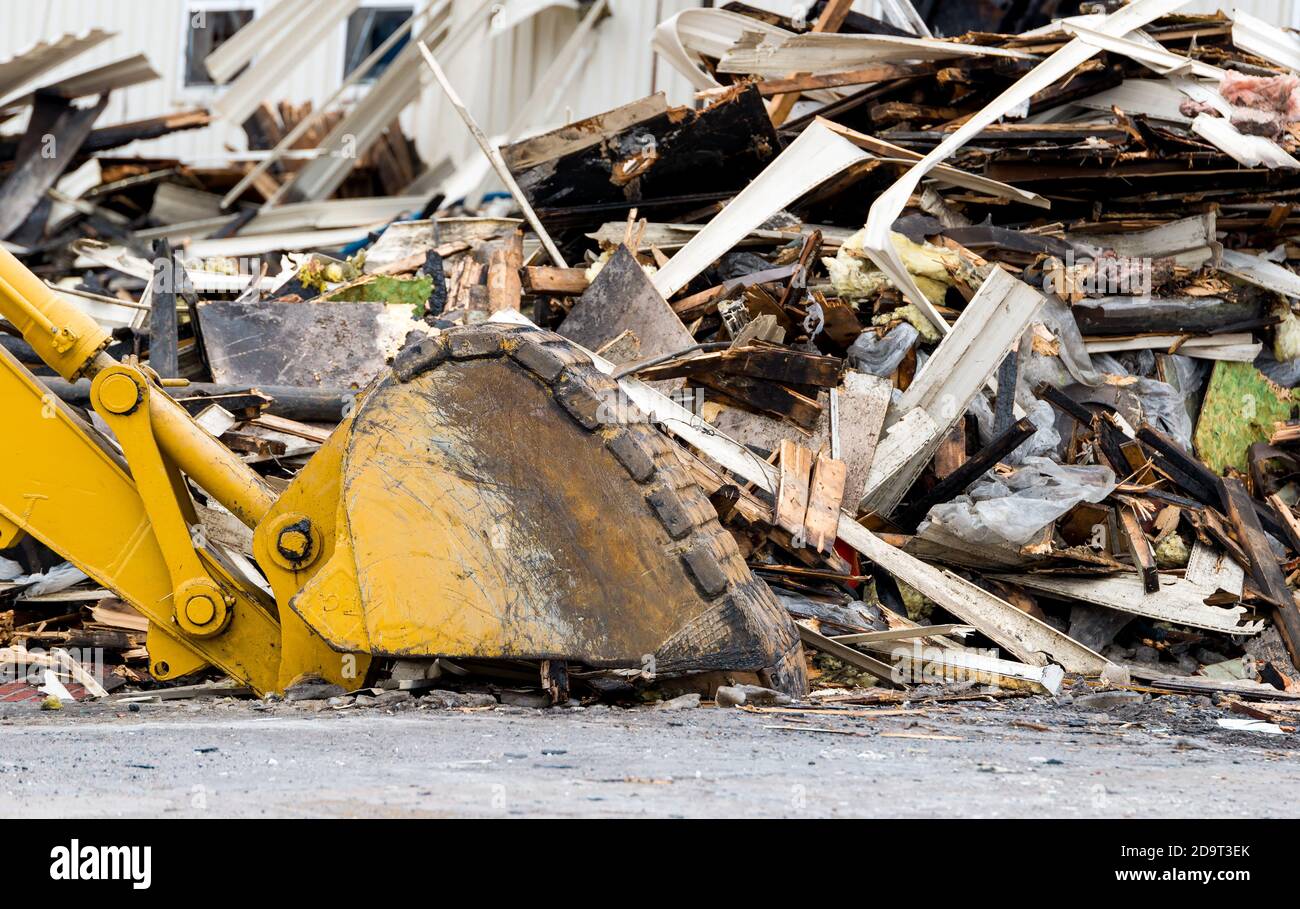 Backhoe bucket next to a pile of debris from a partially demolished building. The bucket is resting upside down on the ground. Focus is on the bucket. Stock Photo