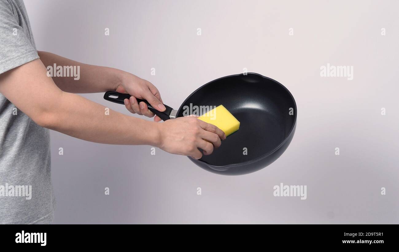 Pan cleaning. Man hand on white background cleaning the non stick pan with  handy dish washing sponge which yellow color on the soft side and green on  Stock Photo - Alamy