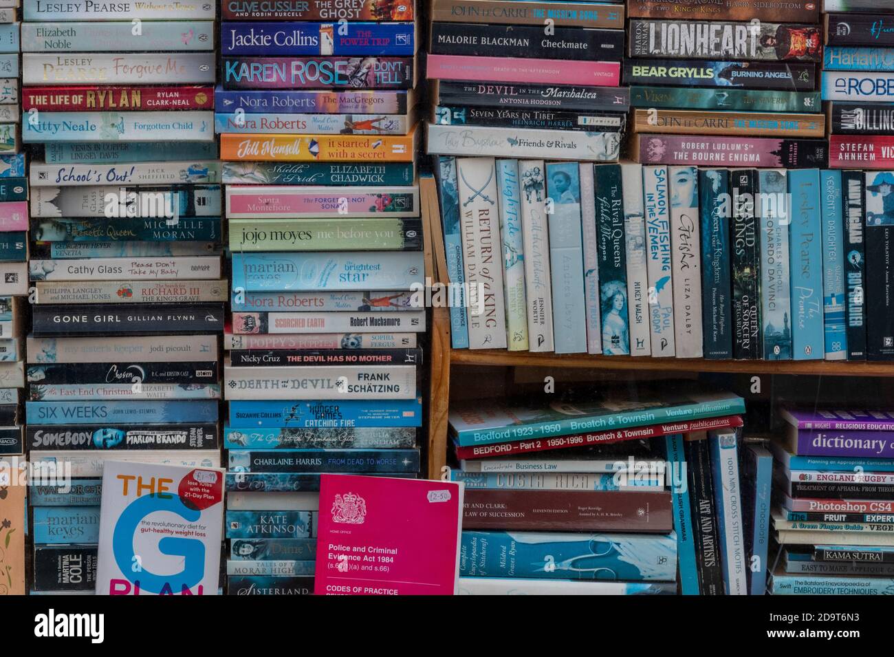 a stack or pile of used paperback books and novels in the window of a used bookshop fading in the sun. Stock Photo
