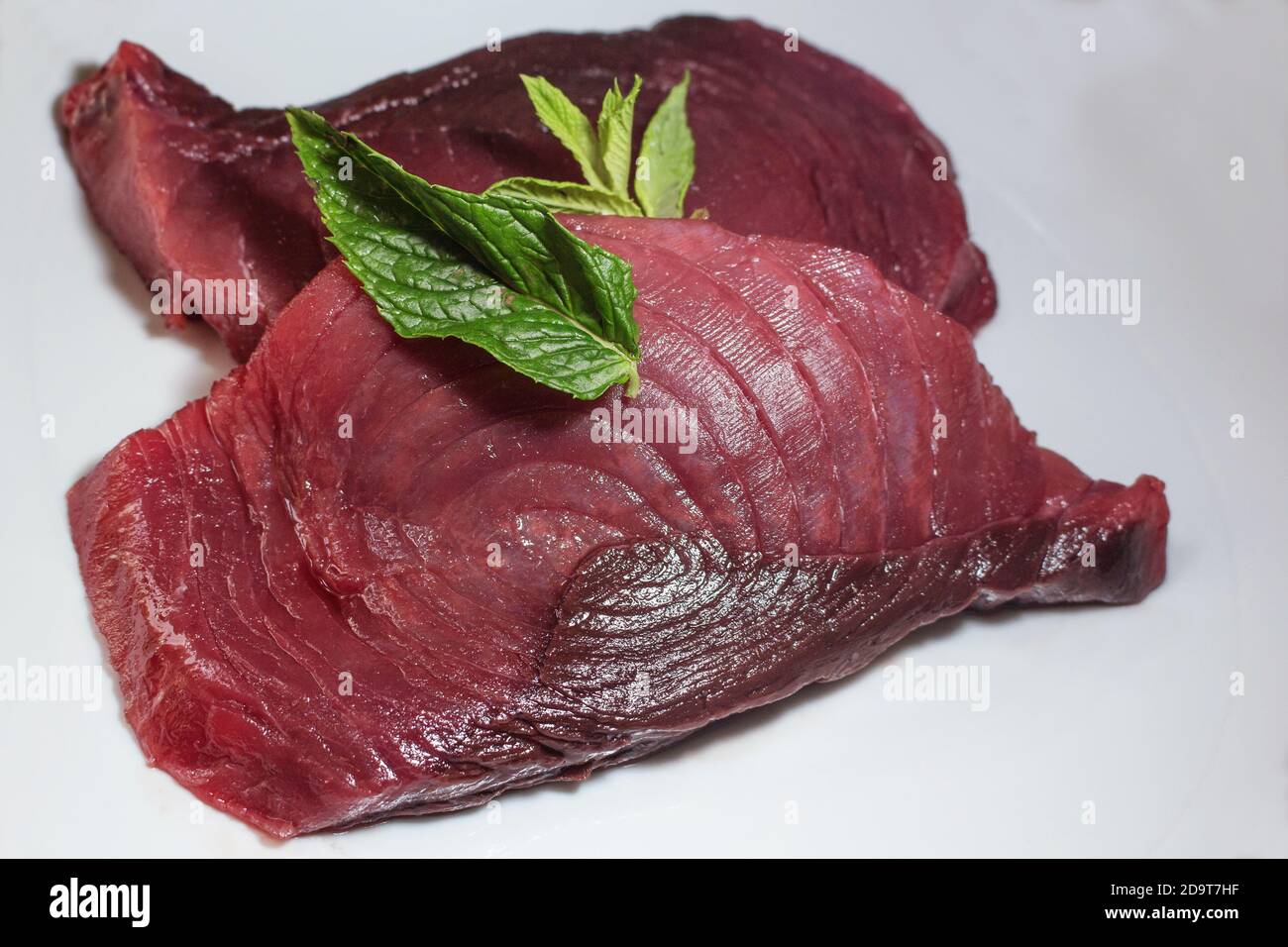 Two slices of raw fresh bluefin tuna on a plate with mint Stock Photo